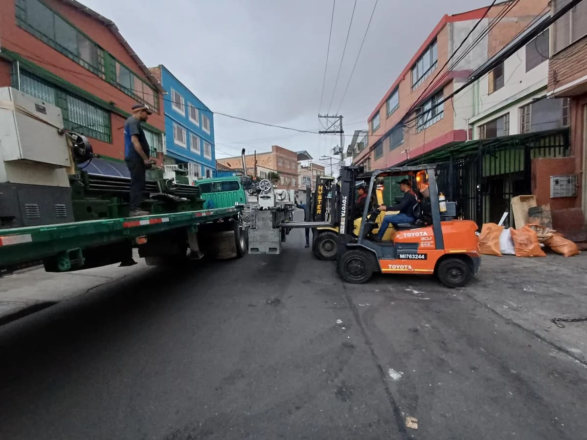 Montacargas cargando equipos pesados sobre un camión en una calle de Bogotá